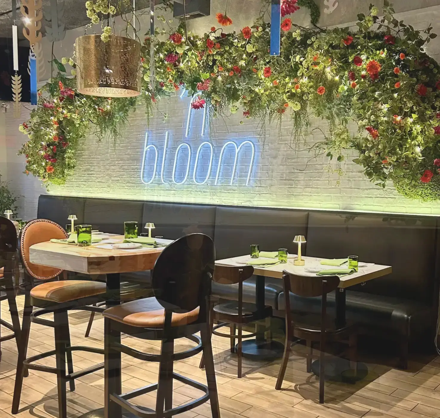 An elegant private event dining room at J. Baldwin's Restaurant, featuring a white brick wall decorated with a neon 'in bloom' sign and lush floral arrangements.