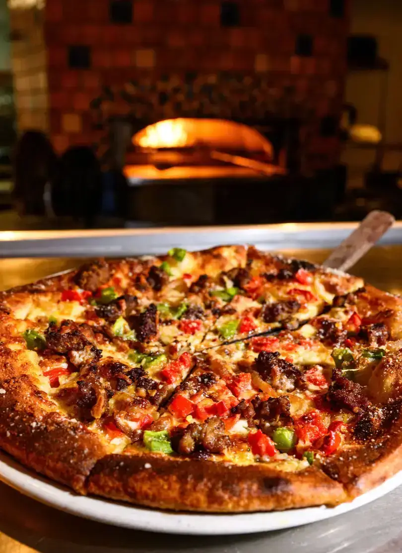 Freshly baked gourmet wood-fired pizza with meat toppings, green bell peppers, and melted cheese, right out of the stone oven at J. Baldwin's.